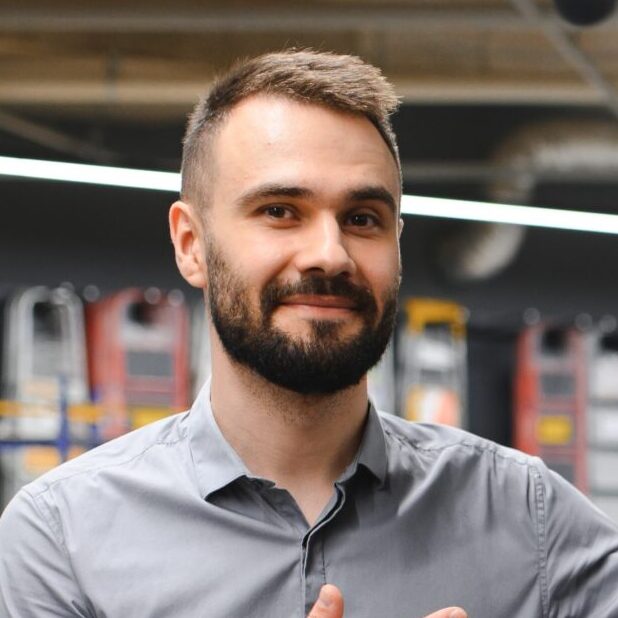 A young man standing in an outdoor power equipment store, smiling confidently.