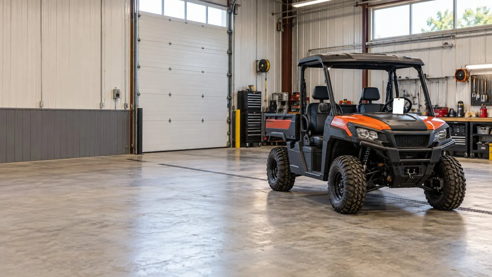 A new utility vehicle parked alone in a clean setup bay with a blank paper tag hanging from the steering wheel, waiting for its customer.